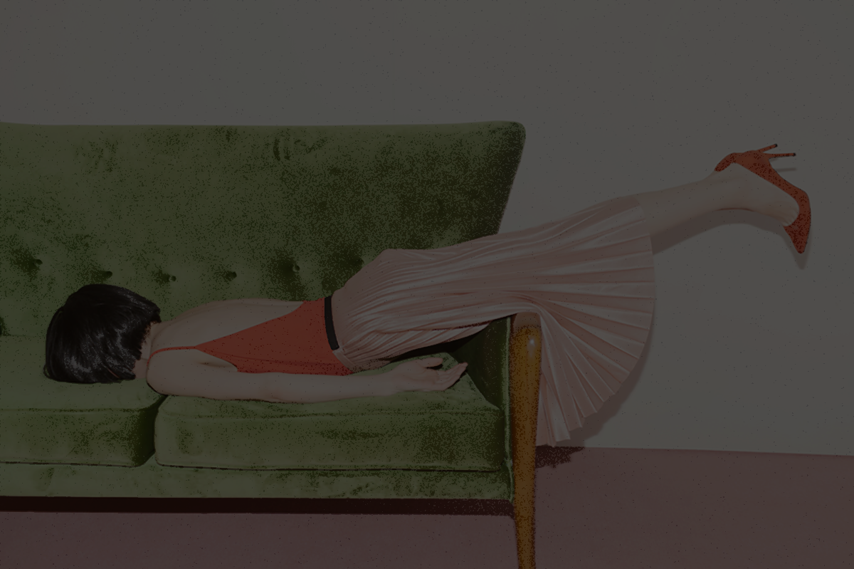 darkened photo of a person in a pink pleated skirt face down on the couch